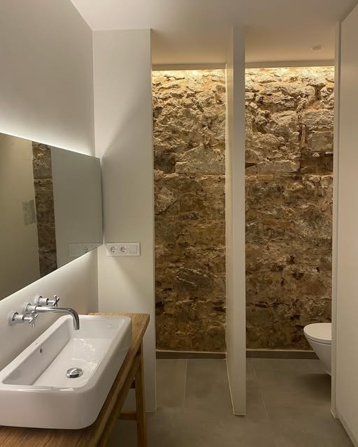Bany amb paret de pedra i il·luminació indirecta