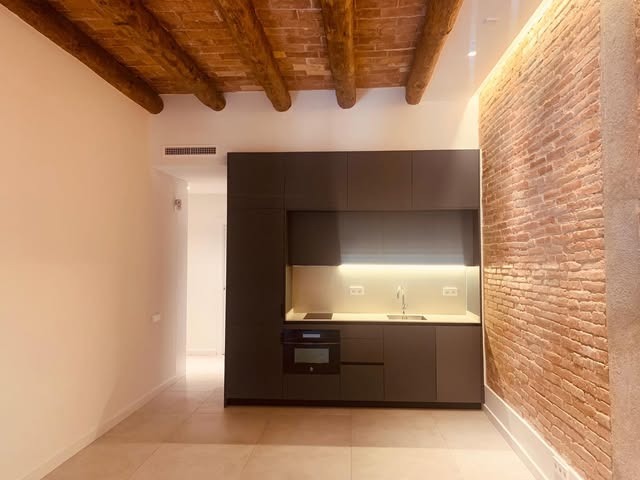 Cuina compacta amb paret de maó vist i bigues